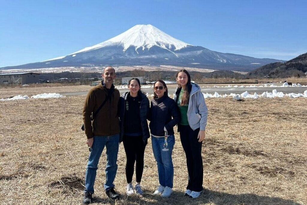 Four tourists enjoy the scenic view of Mount Fuji from a popular viewpoint, capturing memories on a sunny day.