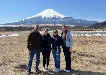 Four tourists enjoy the scenic view of Mount Fuji from a popular viewpoint, capturing memories on a sunny day.