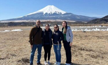 Four tourists enjoy the scenic view of Mount Fuji from a popular viewpoint, capturing memories on a sunny day.